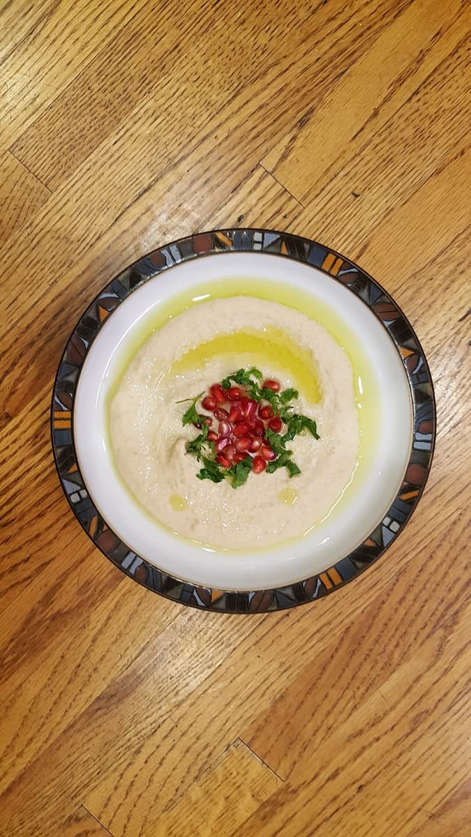 Schüssel mit glattem Kichererbsen- und Sesamdip, garniert mit Öl und Kräutern.