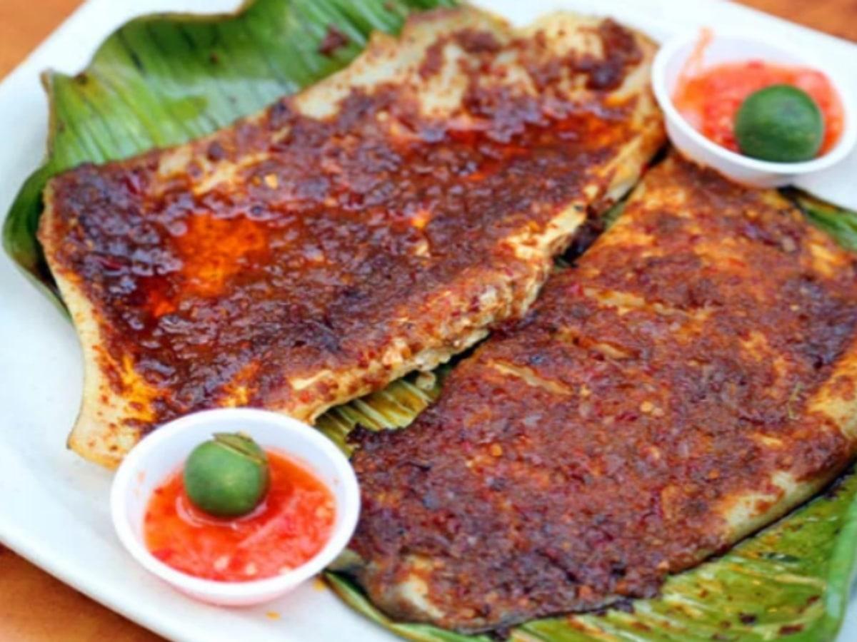 Gegrillter Rochen auf Bananenblatt, bedeckt mit dunkelrotem Sambal und serviert mit Limettenhälften.
