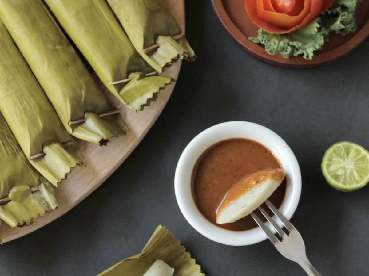Paquets de feuilles contenant de la pâte de poisson épicée servis avec une sauce et du citron vert.
