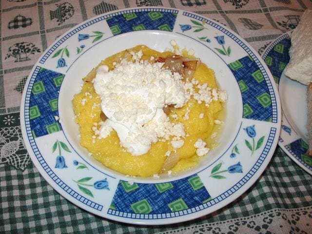 Gelber Polenta-Brei, belegt mit zerbröckeltem Käse und saurer Sahne auf einem Teller.