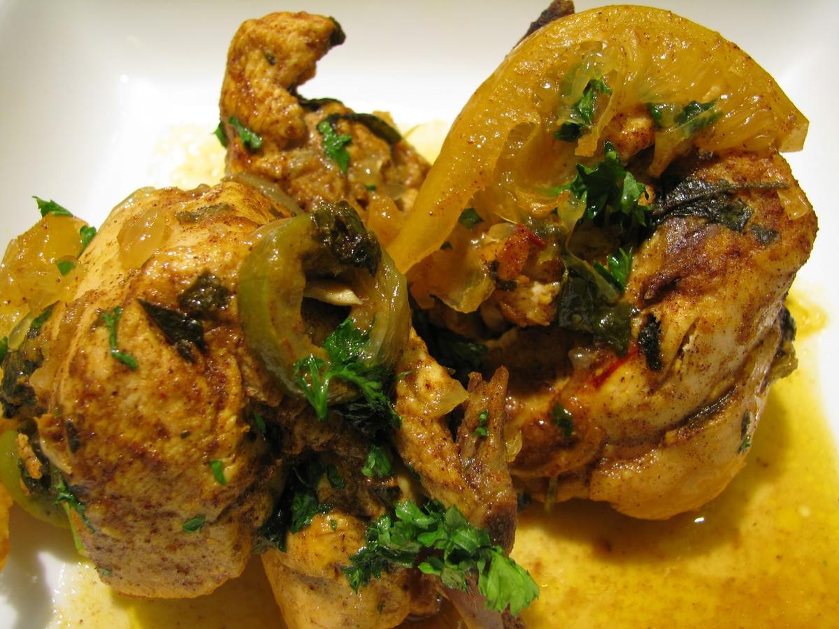 Hühnchenstücke in gelber Sauce mit eingelegter Zitrone, Oliven und Kräutern.