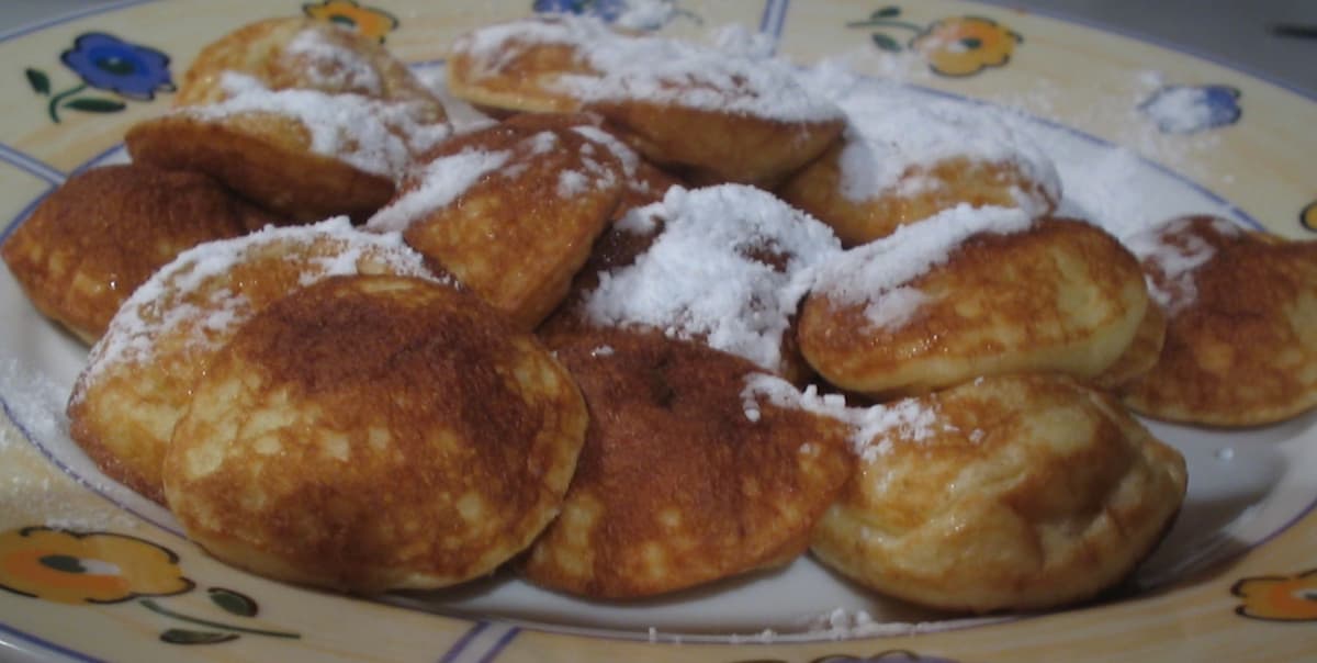 Pequeños panqueques inflados espolvoreados con azúcar en polvo en un plato.