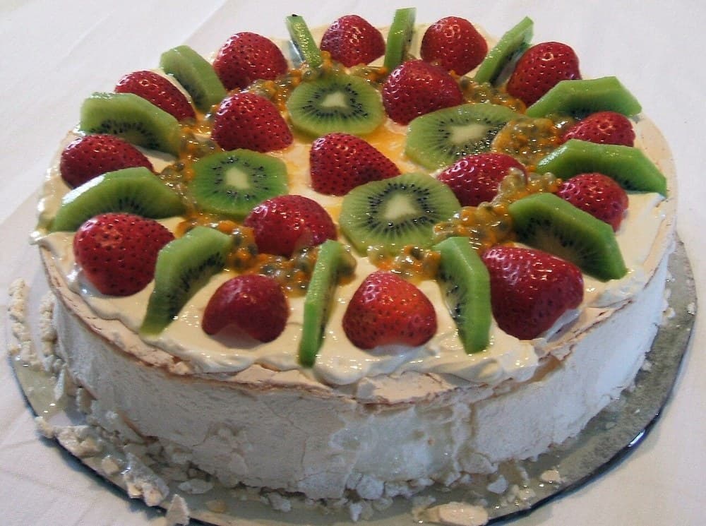 Rundes Baiser-Dessert, belegt mit Sahne, Kiwi, Erdbeeren und Passionsfrucht.