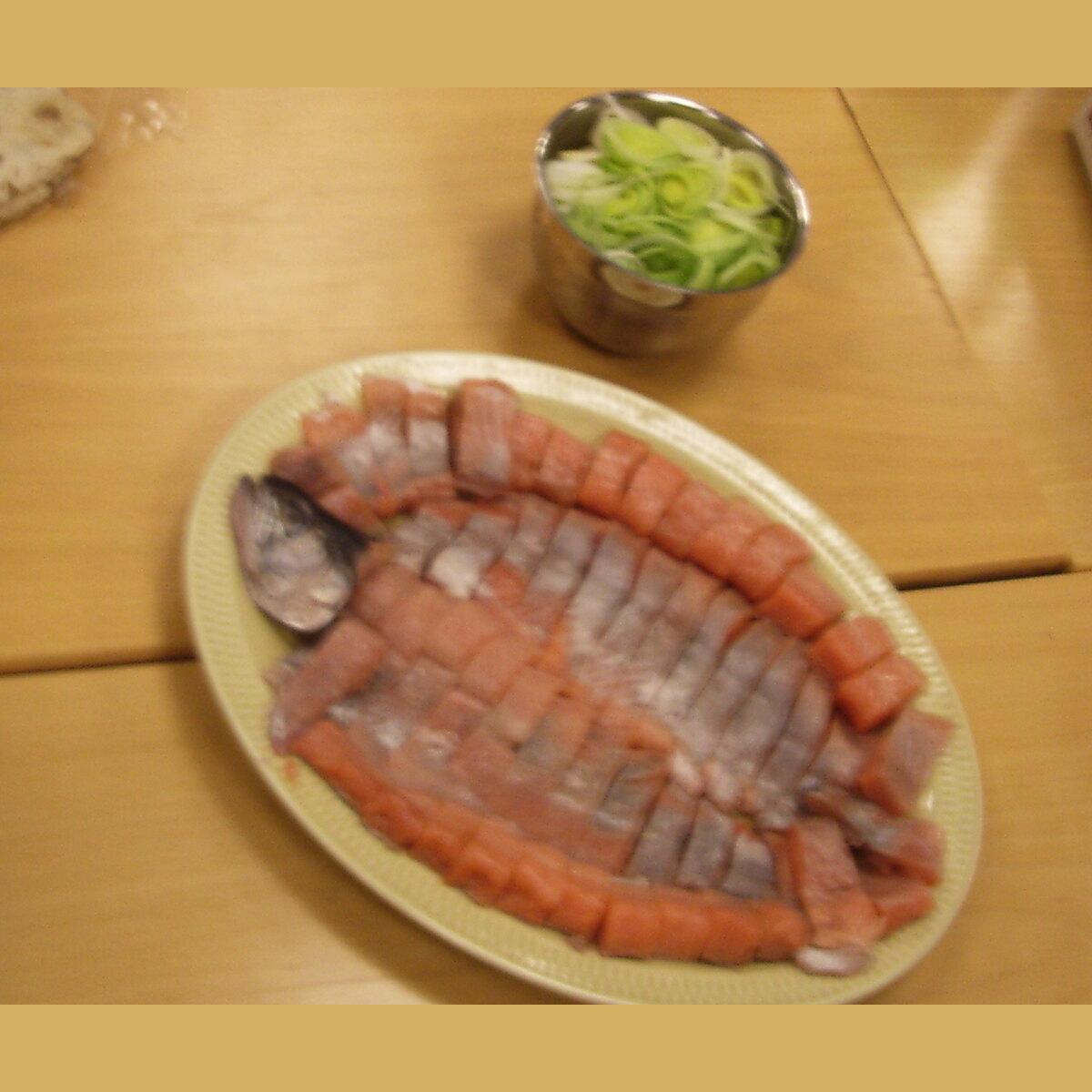 Teller mit dünn geschnittenem rosa und silbernem Fisch mit einer kleinen Schüssel geschnittener Lauch in der Nähe.