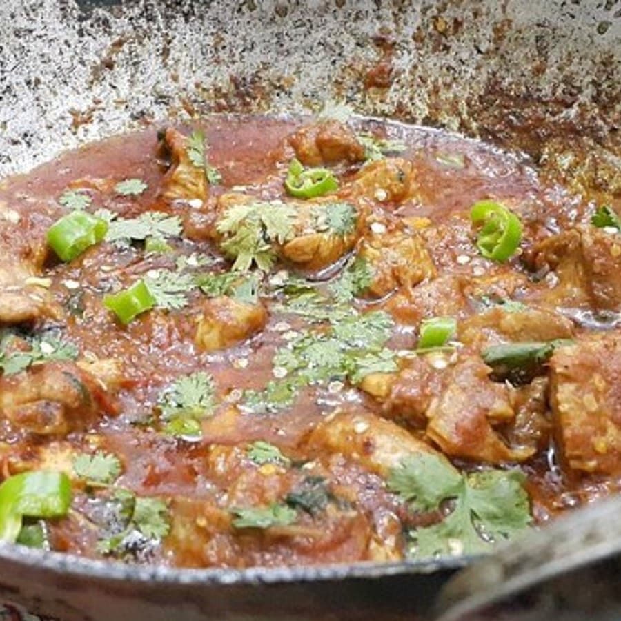 قطع دجاج في صلصة غنية بالطماطم داخل مقلاة كراهي معدنية.