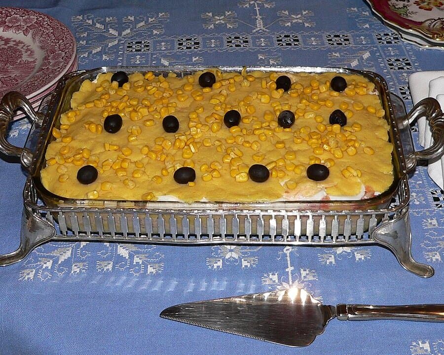 Rechteckiges Tablett mit gelbem Schichtgericht aus Kartoffeln, belegt mit schwarzen Oliven.