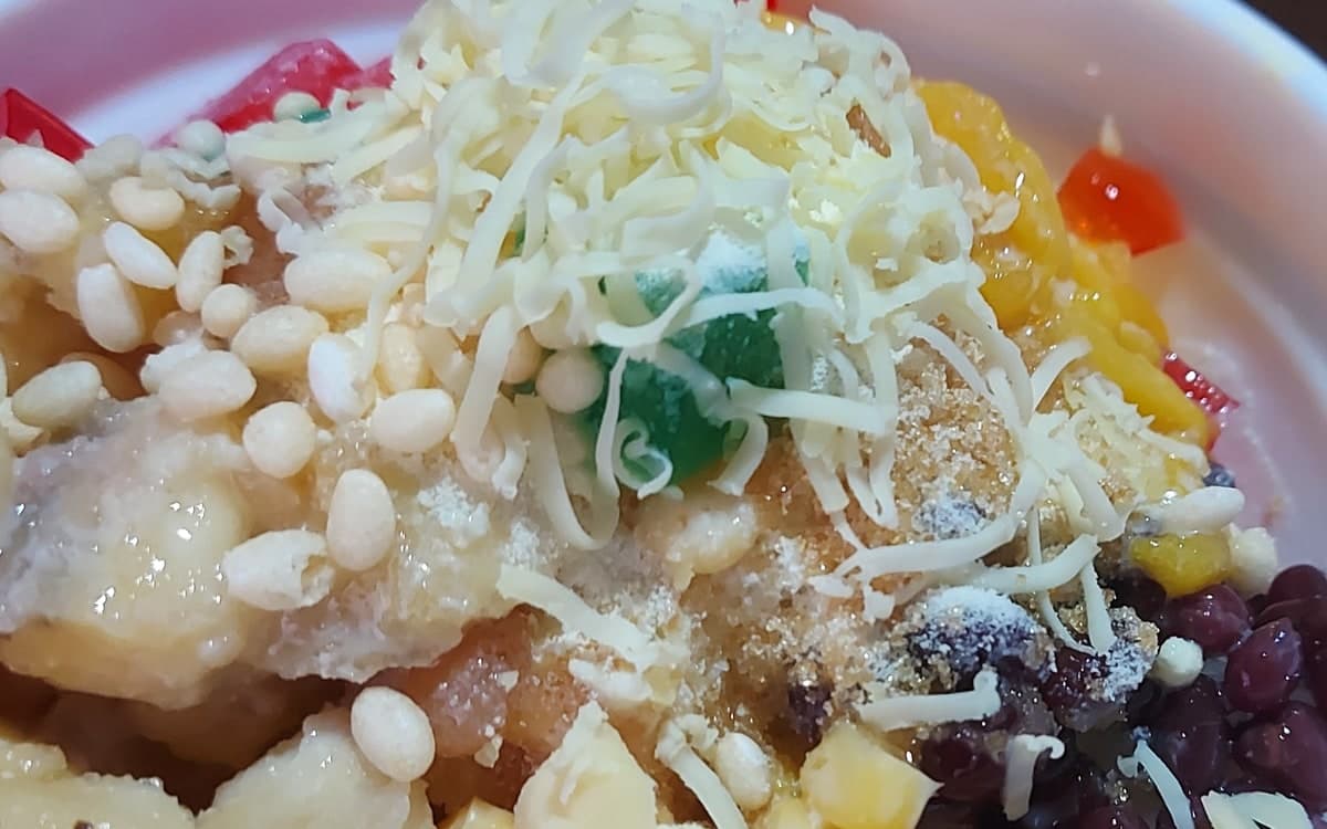 Nahaufnahme einer Schüssel mit Eisraspeldessert mit Obst, Bohnen, Geleewaren und geriebenem Topping.
