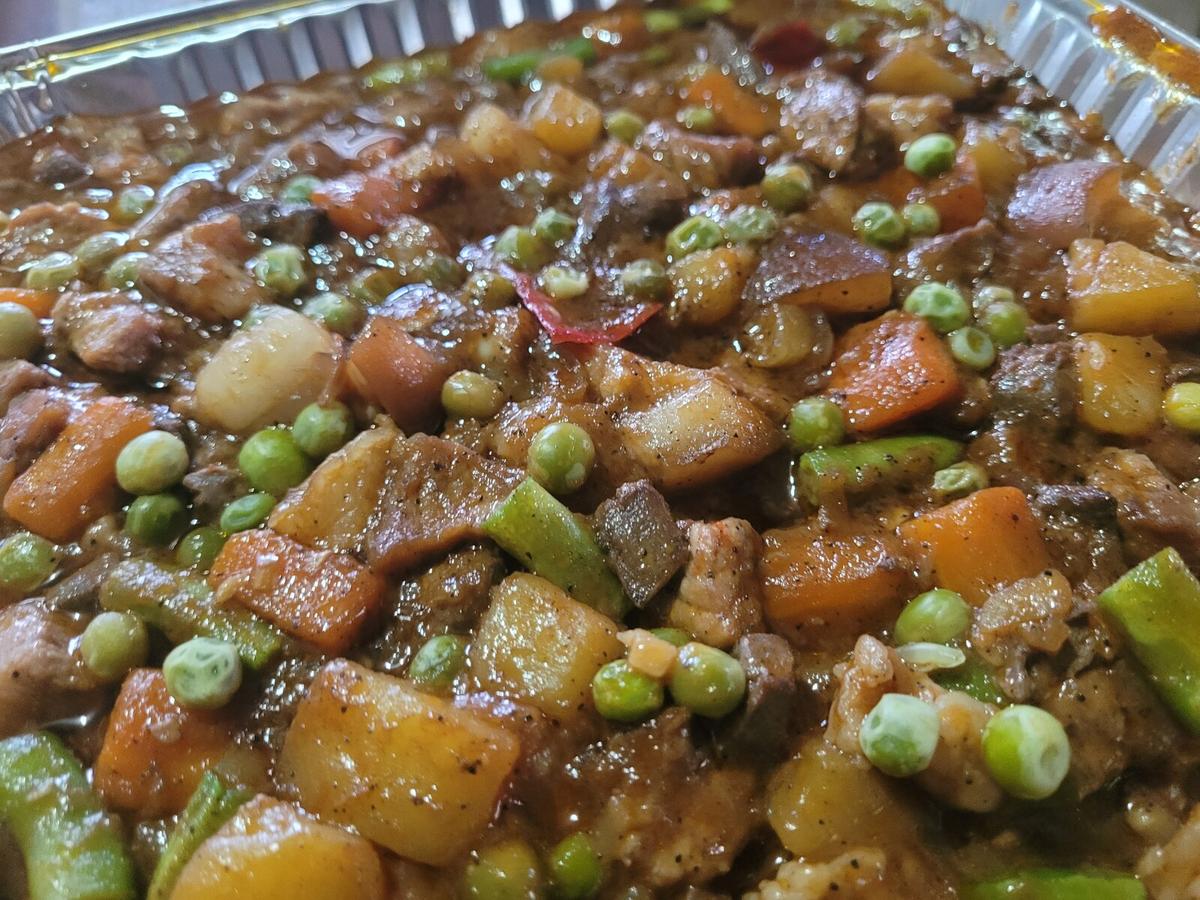 Tomatenbasierter Schweineeintopf mit gewürfelten Kartoffeln, Karotten und Paprika in einer Aluminiumschale.