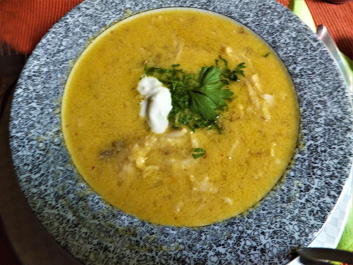 Schüssel mit cremiger gelber Tripe-Suppe, garniert mit Kräutern und einem Löffel Sauerrahm.