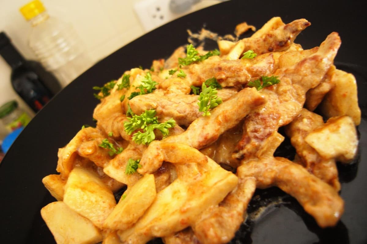 Potongan daging sapi dengan saus krim disajikan dengan kentang di piring hitam.