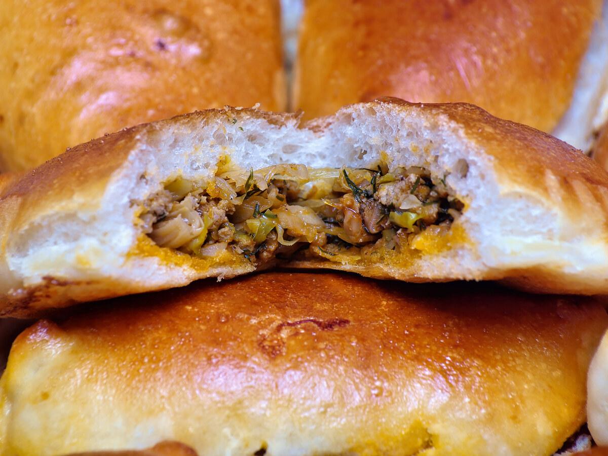 Goldene gefüllte Brötchen, eines aufgeschnitten, um die herzhafte Füllung zu zeigen.
