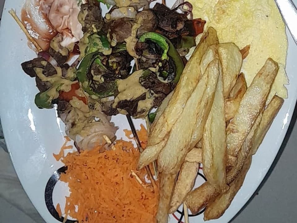 قطع اللحم المشوية مع البصل وشرائح الخضار والبطاطا المقلية في طبق.