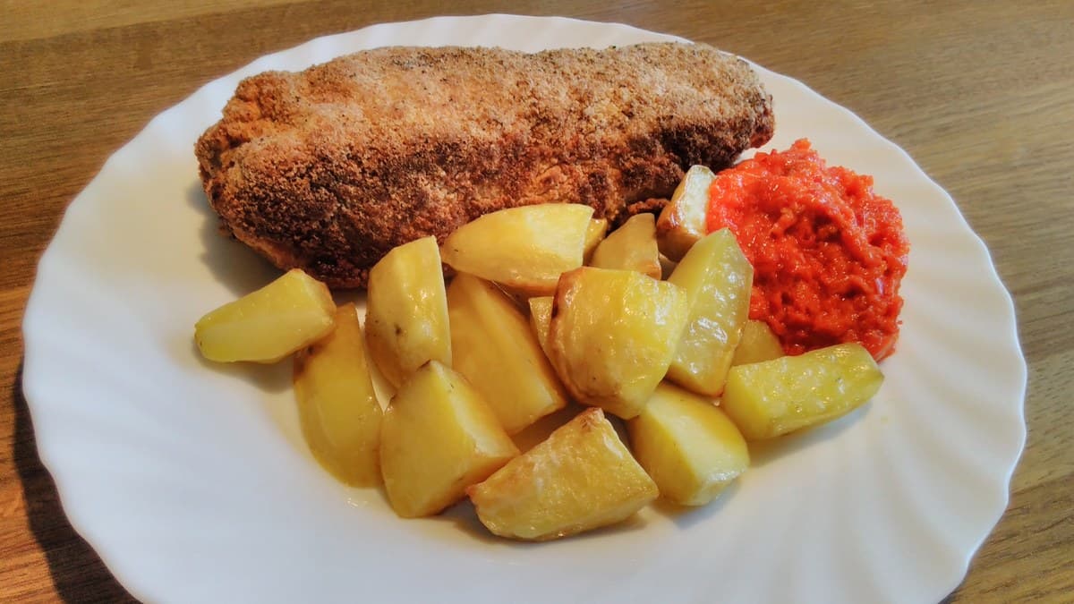 Paniertes, aufgerolltes Schnitzel mit Kartoffeln und roter Soße auf weißem Teller.