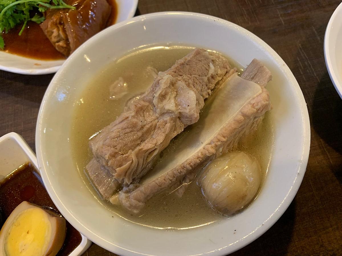 Schale mit klarer Schweinerippchensuppe, einem großen Rippenstück und heller Brühe.