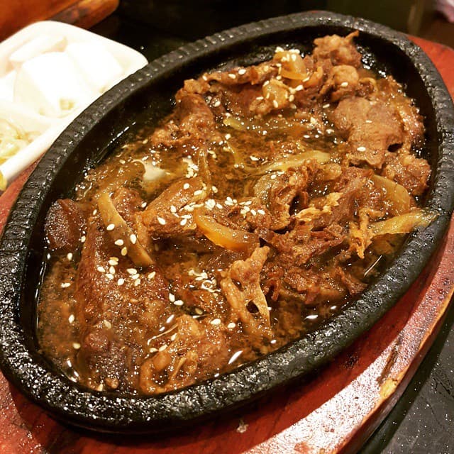 Cooked marinated beef slices with onions and sesame seeds in a dark serving dish.