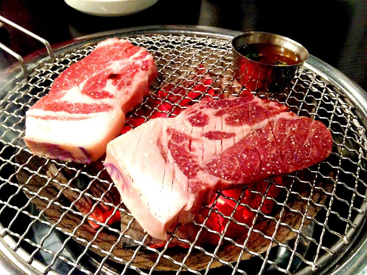 Thick pork slices cooking over a small tabletop charcoal grill with a sauce cup nearby.