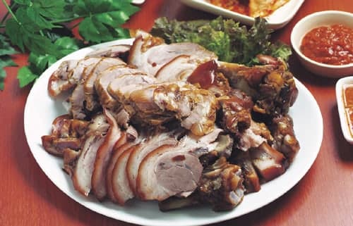 In Scheiben geschnittene geschmorte Schweinefüße auf einer Platte mit Grünzeug und Dip.