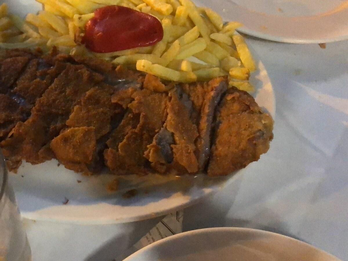 Aufgeschnittenes paniertes Kalbsschnitzel mit Pommes auf einem Teller.