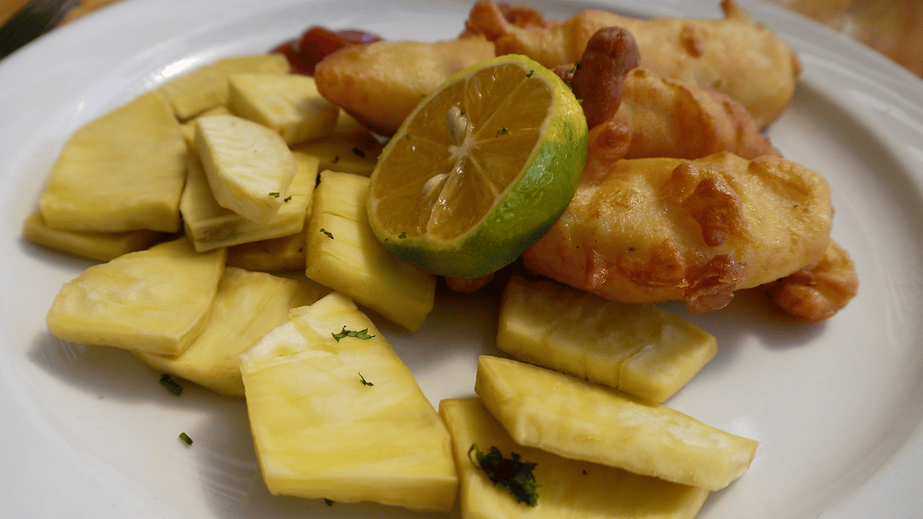 Frittierte Fischstücke mit Brotfruchtstücken und Limette auf einem Teller.