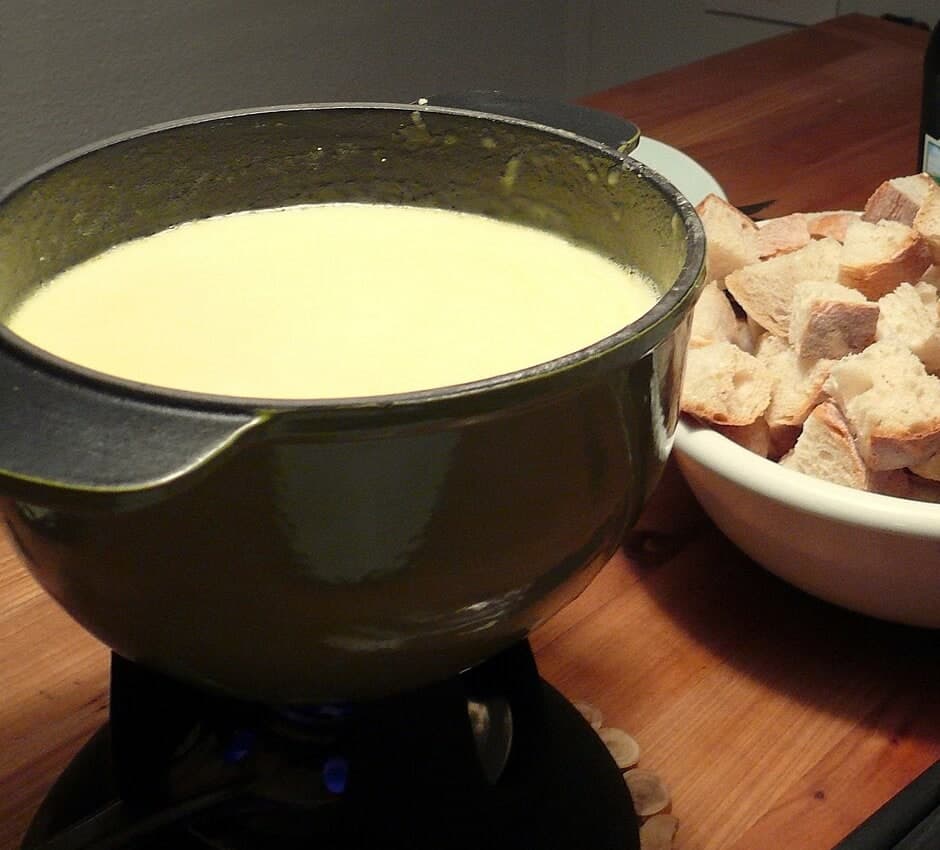 Geschmolzenes Käsefondue in einem Topf neben einer Schüssel mit Brotwürfeln.
