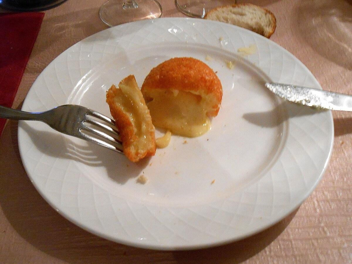 Frittierter Käsekrapfen, aufgeschnitten auf weißem Teller.