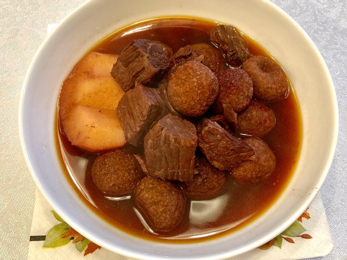 Schüssel mit Kibbeh-Bällchen und Fleischstücken in rötlicher Brühe mit hellen Quittenstücken.