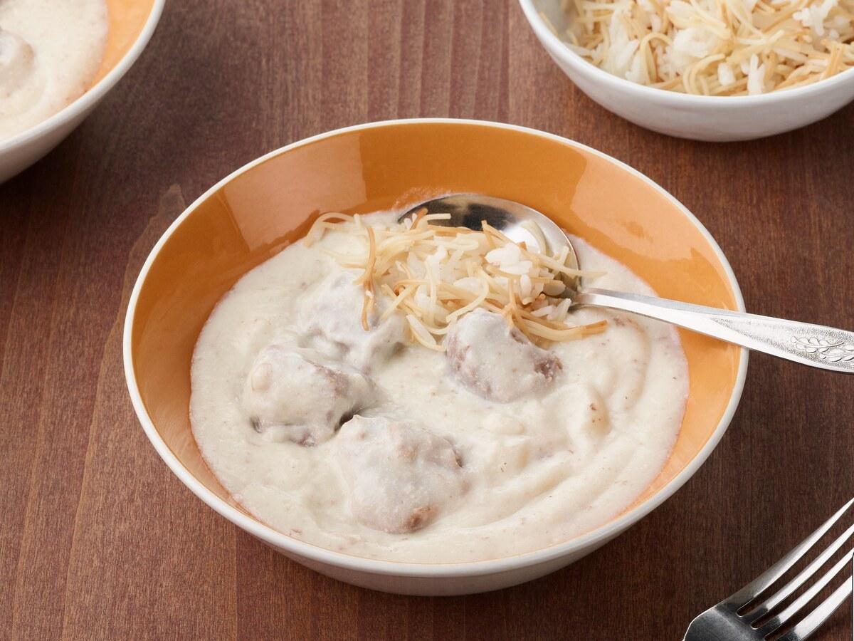 Schüssel mit Lammstücken in weißer Joghurtsauce, daneben Vermicelli-Reis.