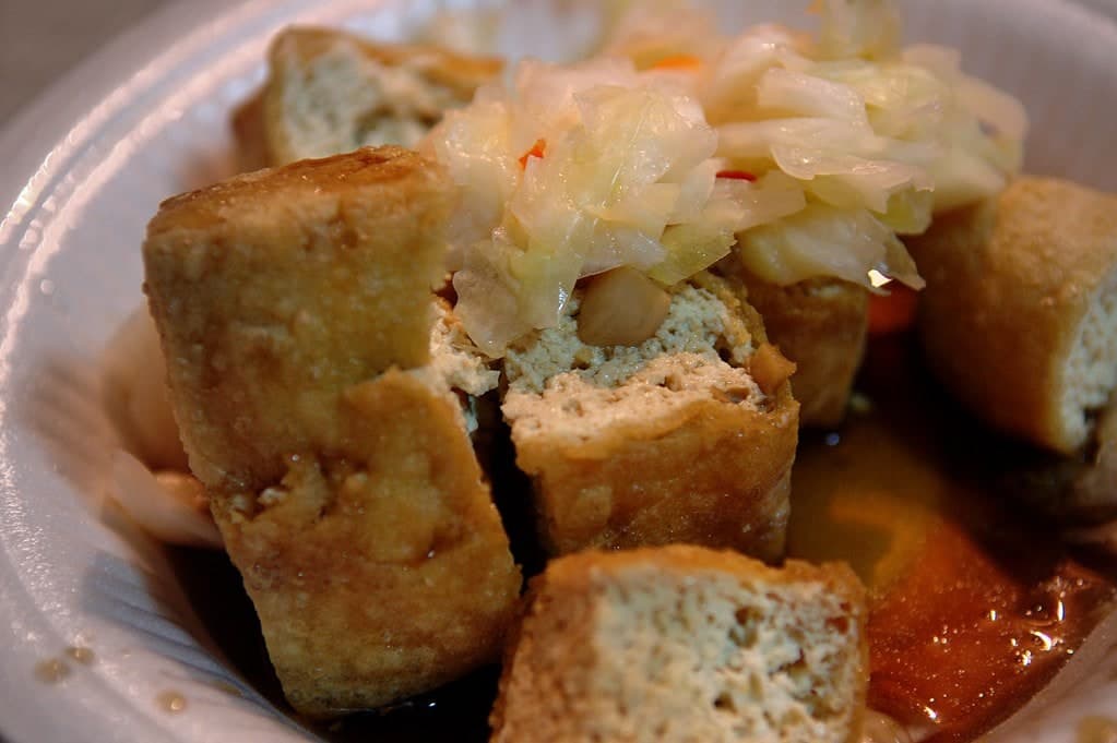 Frittierte Tofuwürfel mit eingelegtem Kohl und Soße in einer flachen Schale.