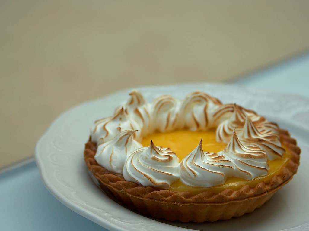 Eine Zitronenpudding-Tarte mit geröstetem Baiser auf einem weißen Teller.
