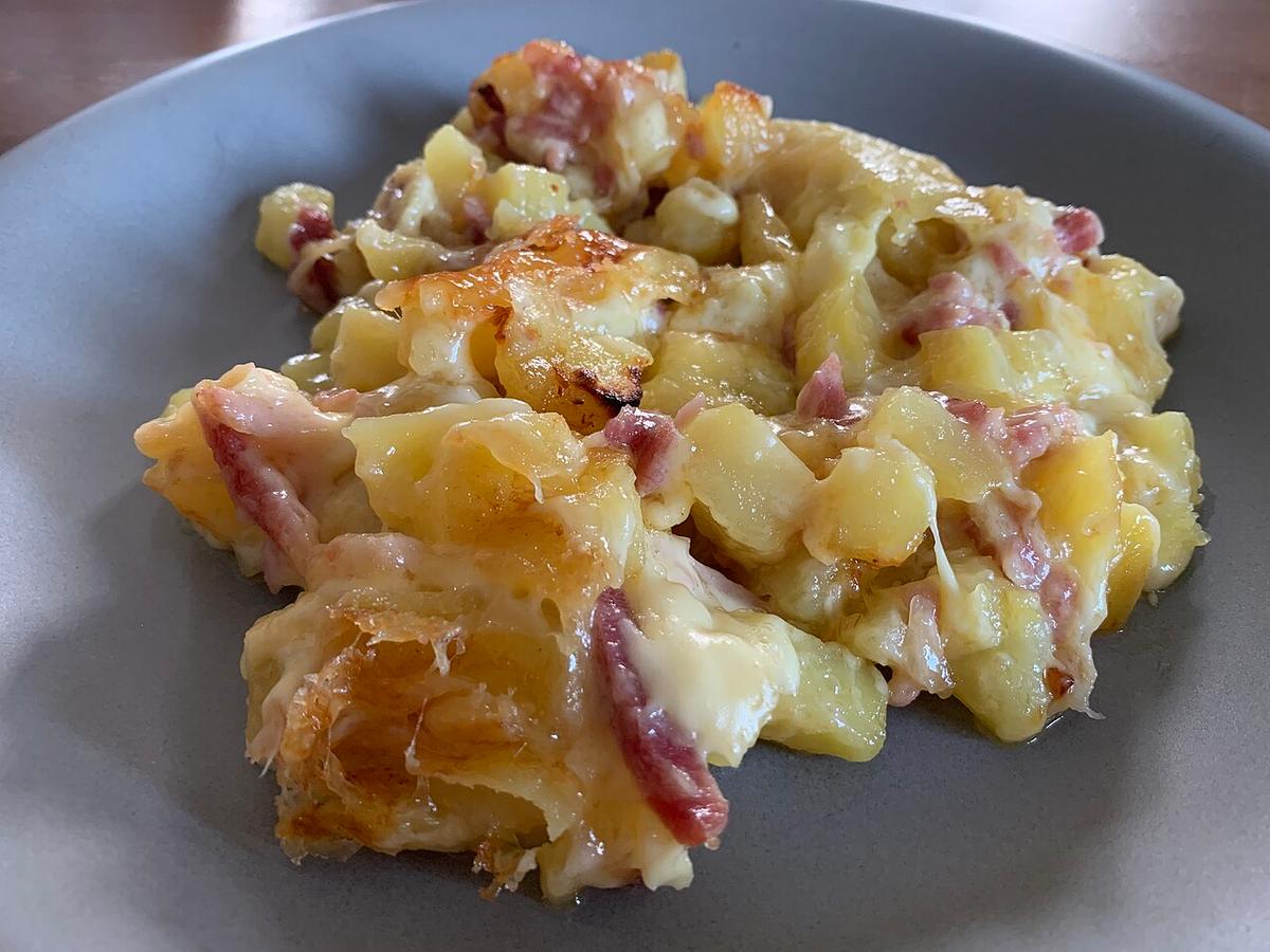 Käse-Kartoffelgratin mit Speckstücken auf einem grauen Teller serviert.
