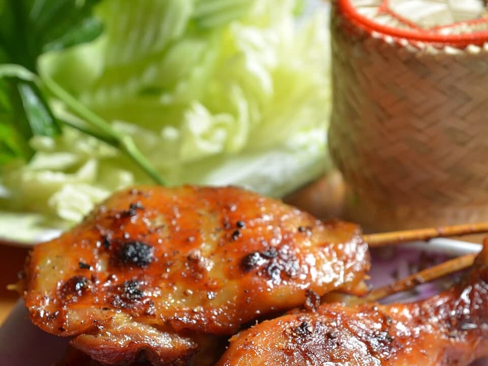 Gegrillte Hühnchenteile serviert neben Kohl und einem kleinen Korb mit Klebreis.