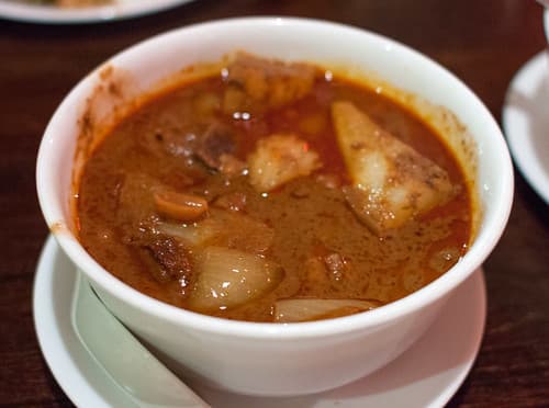Schüssel mit rötlichem Kokos-Curry mit Kartoffeln und Fleisch.