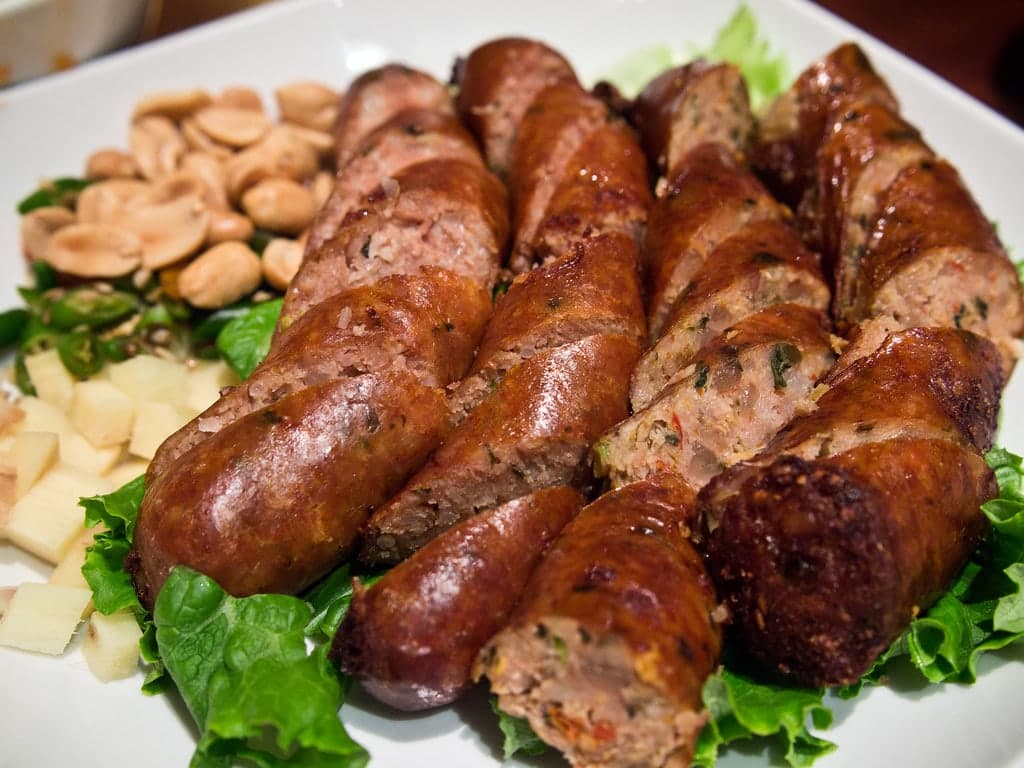 Geschnittene gegrillte Kräuter-Schweinswurst auf einem Teller mit Gemüse.