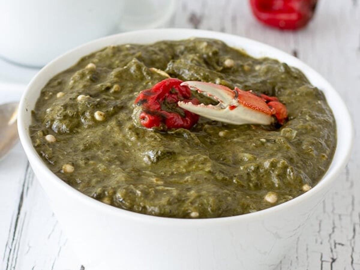 Tazón de sopa verde espesa de hojas con semillas de okra y una pinza de cangrejo como adorno.