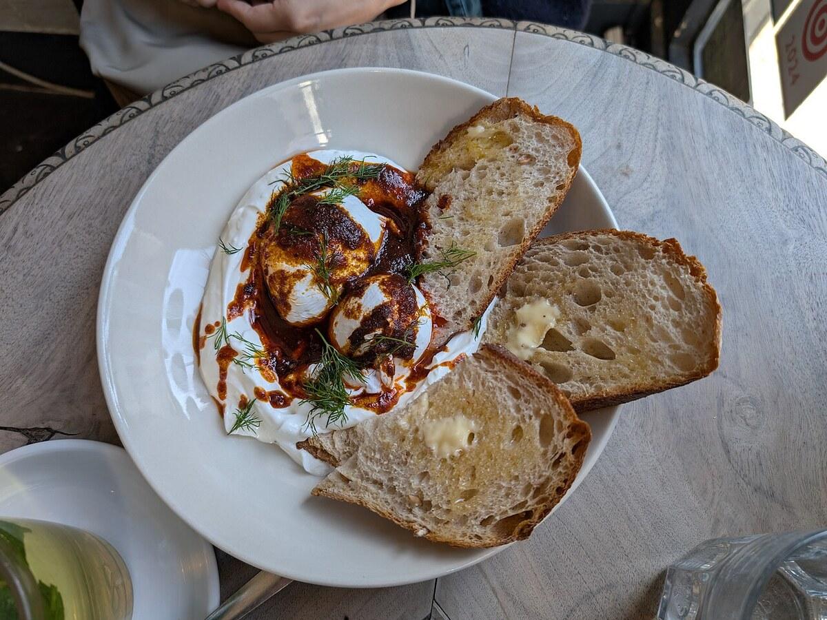 Teller mit pochierten Eiern in Joghurt, roter Paprikabutter und Brotscheiben.