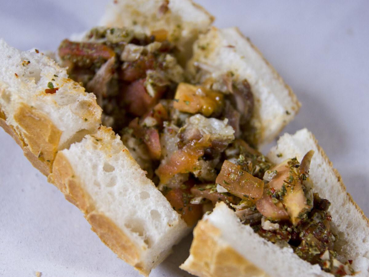 Offenes Brotsandwich gefüllt mit gehacktem Grillfleisch, Gewürzen, Tomate und Kräutern.