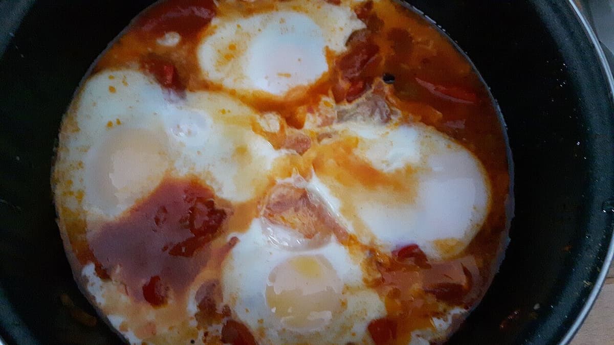 Eier in Tomaten- und Paprikasauce in einer dunklen Pfanne.