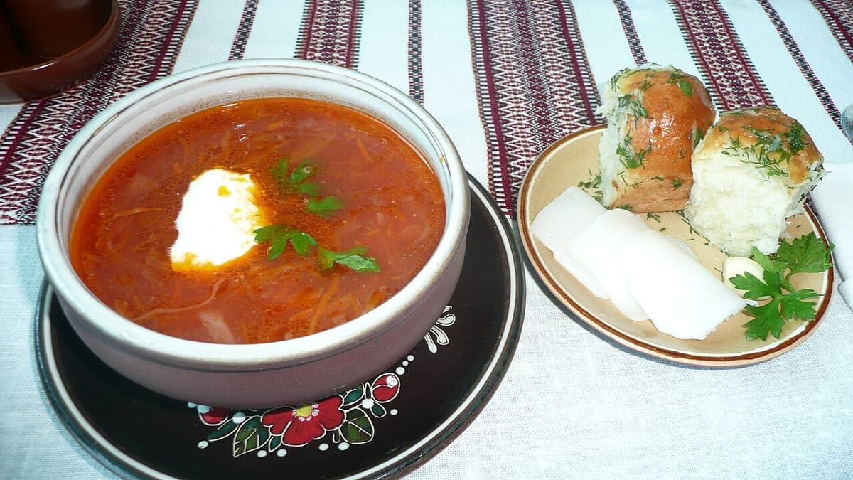 Schüssel mit roter Rübensuppe mit Sauerrahm und Knoblauchbrötchen auf einem Nebenteller.