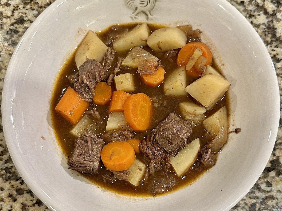 Tazón de guiso con trozos de carne, patatas, zanahorias y caldo oscuro.