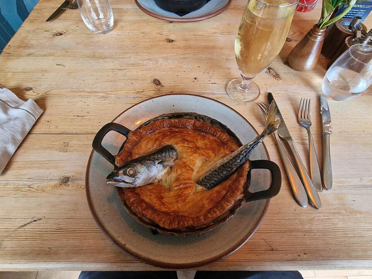 Runder Teigkuchen mit kleinen Fischköpfen, die durch die Kruste in einer Servierschale ragen.