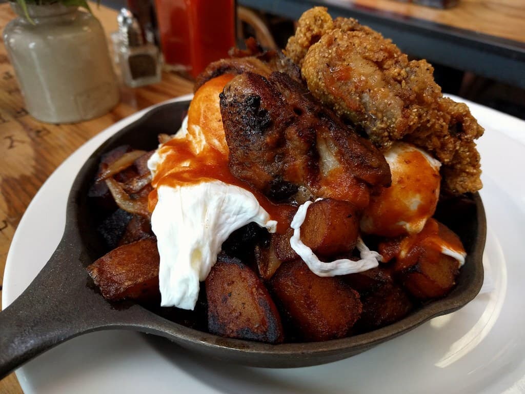 Pfannenartiges Eiergericht mit frittierten Austern, Speck, Kartoffeln und Soße auf einem Restauranttisch.