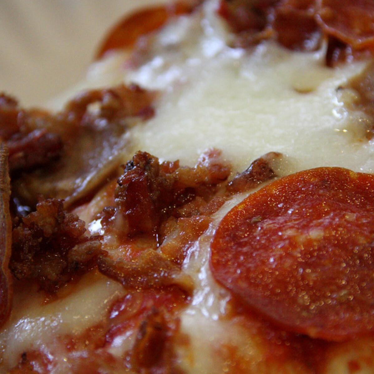 Primer plano de una porción de pizza de pepperoni de masa delgada con queso derretido.