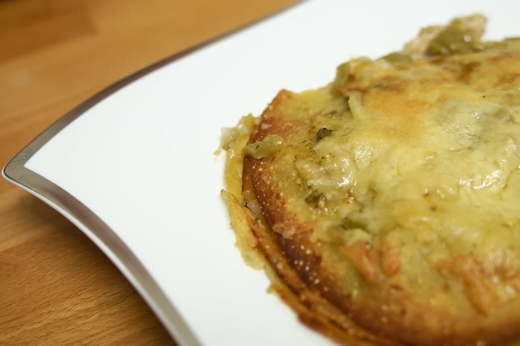 Gestapelte Tortillas mit grüner Chilisauce und geschmolzenem Käse auf einem Teller.