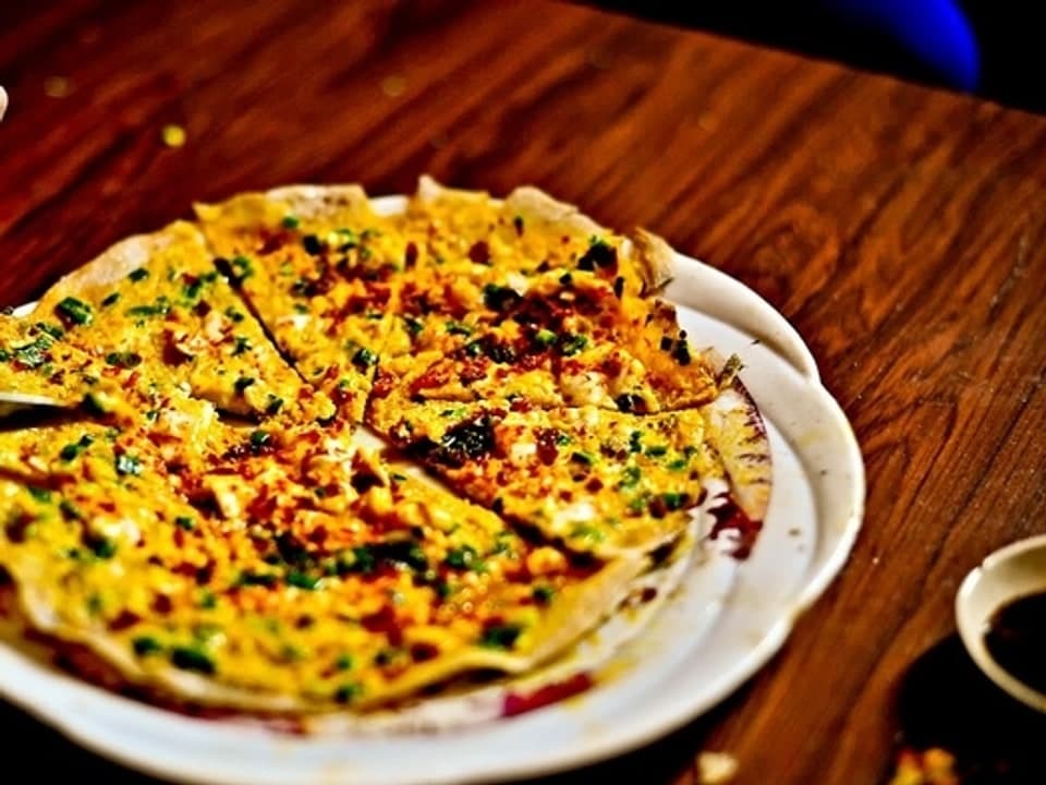 Gegrillte Reispapier-Runde mit Ei, Frühlingszwiebeln, getrockneten Garnelen und Chilisauce belegt.